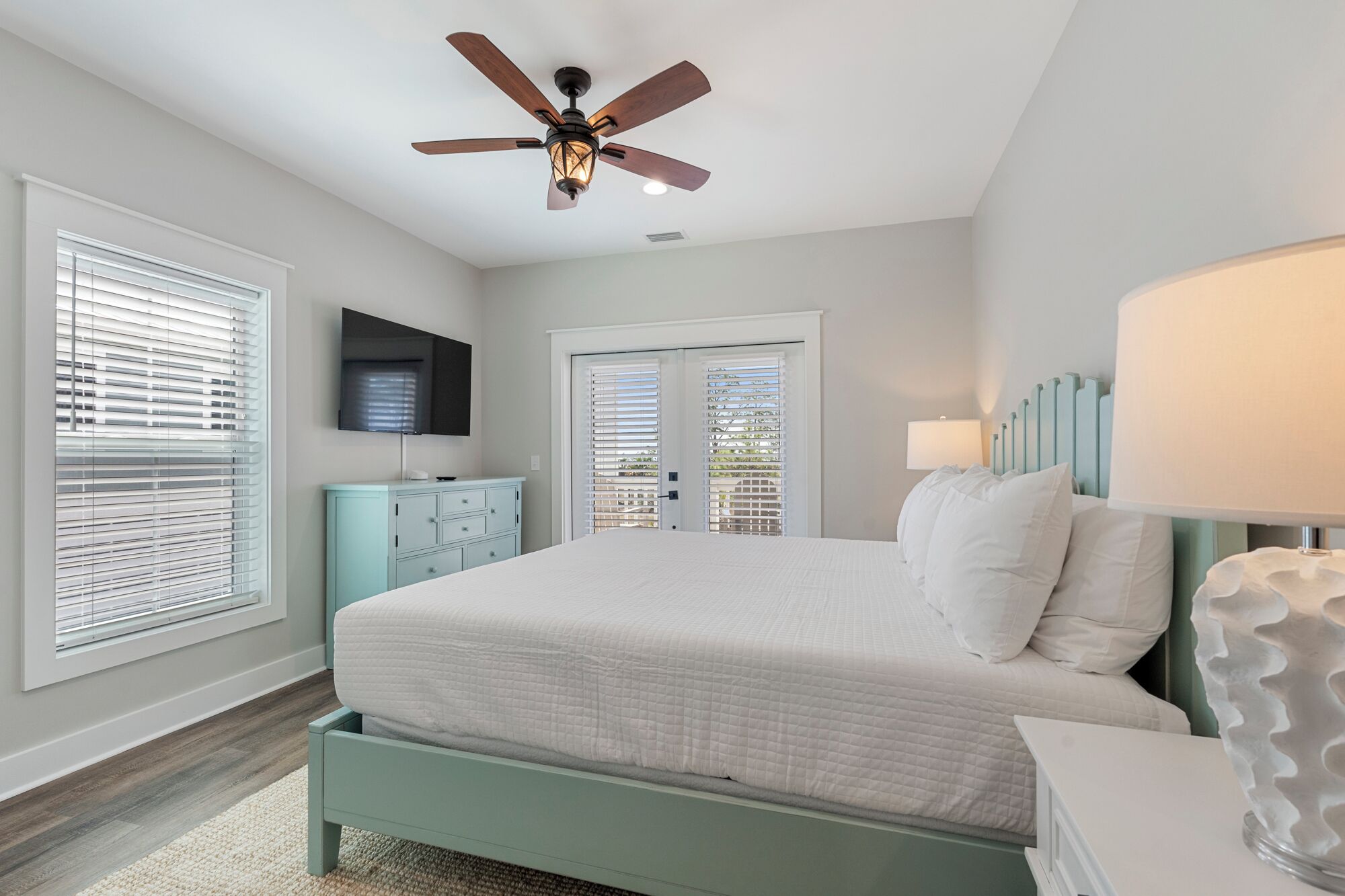 A bedroom with a bed, a ceiling fan, a TV, and a window with blinds.