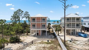 A beachfront property with two multi-story buildings, a sandy pathway, and a clear view of the ocean.