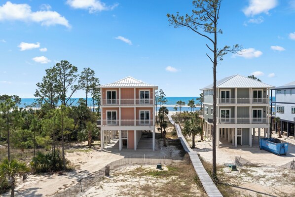 Une propriété située en bord de mer, comprenant deux immeubles à plusieurs étages, un sentier sablonneux et une vue dégagée sur l’océan.