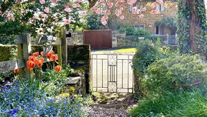 Un jardin avec une porte en bois, des plantes en fleurs et un bâtiment en pierre en arrière-plan.
