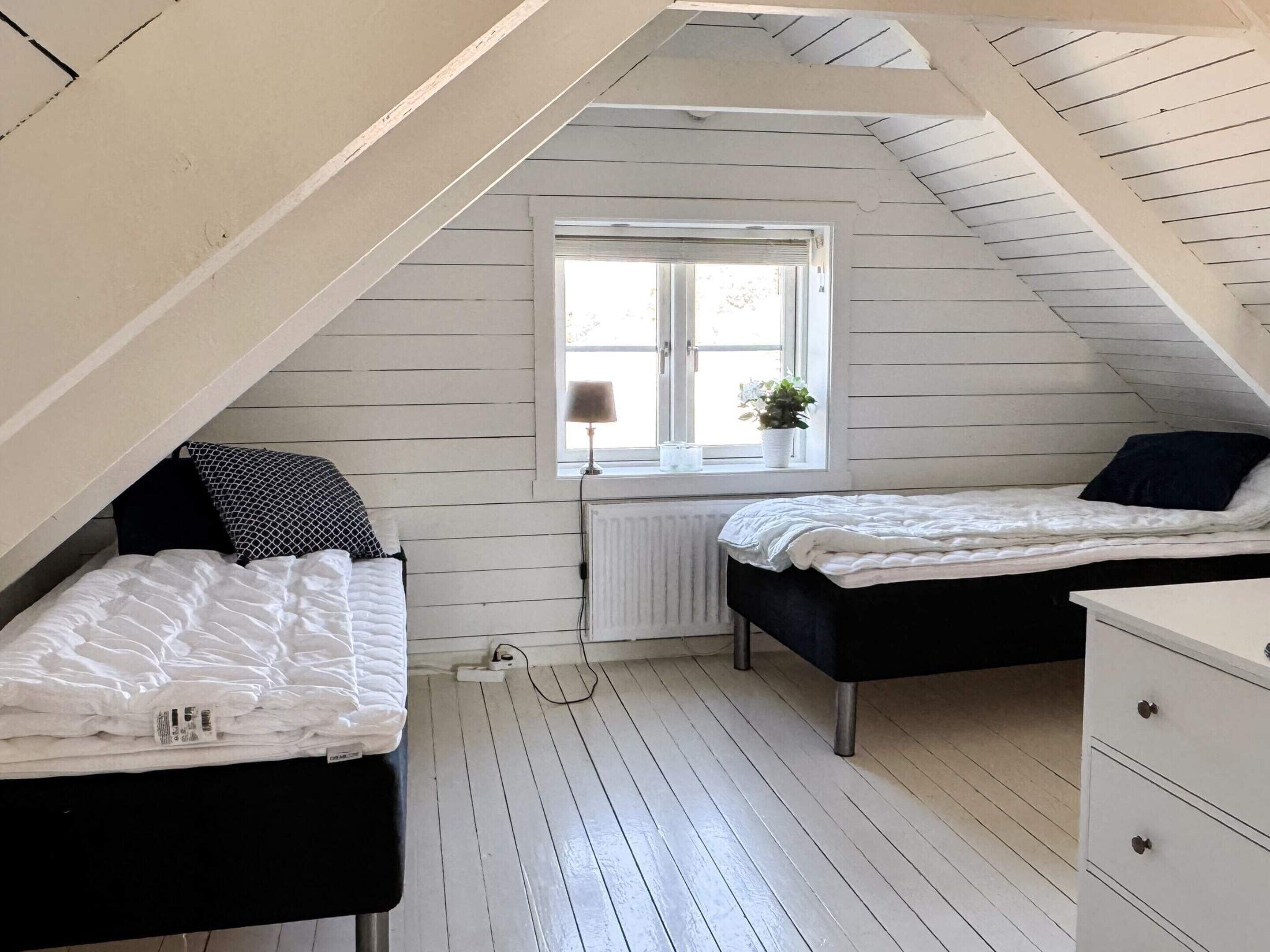 Ett litet sovrum på vinden med två sängar, ett fönster med en blomma i och ett element.