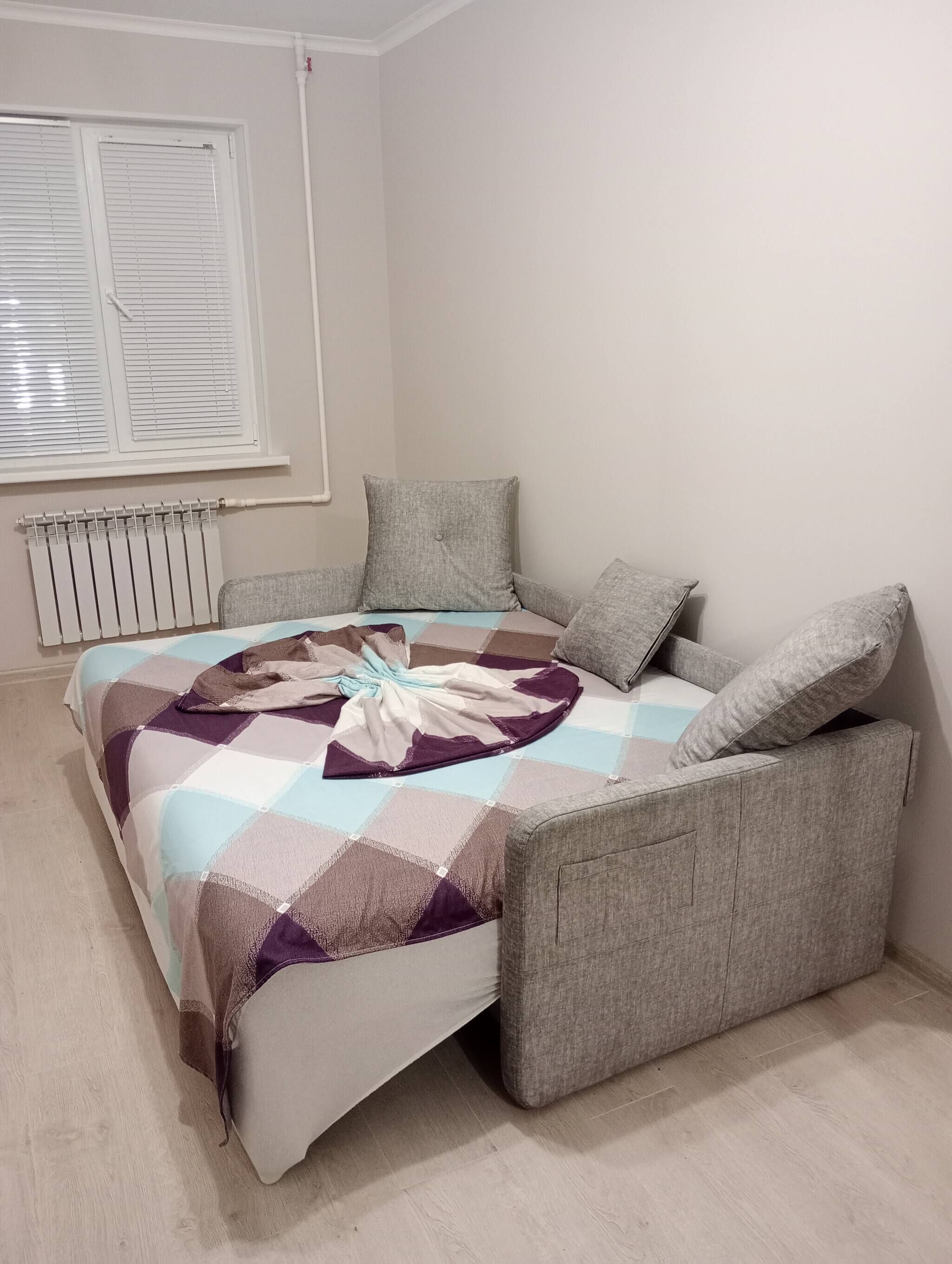 A bedroom with a bed, grey upholstered headboard, and a radiator.
