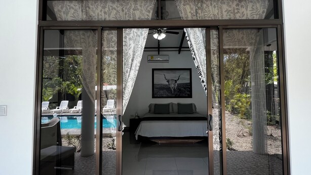 A modern bedroom with a bed, a ceiling fan, and a view of a pool and outdoor area. - Casa Lassie, private pool, high speed Wifi (Cahuita)