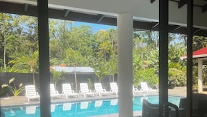 A pool area with tiled flooring, lounge chairs, and a view of lush greenery. - Casa Lassie, private pool, high speed Wifi (Cahuita)