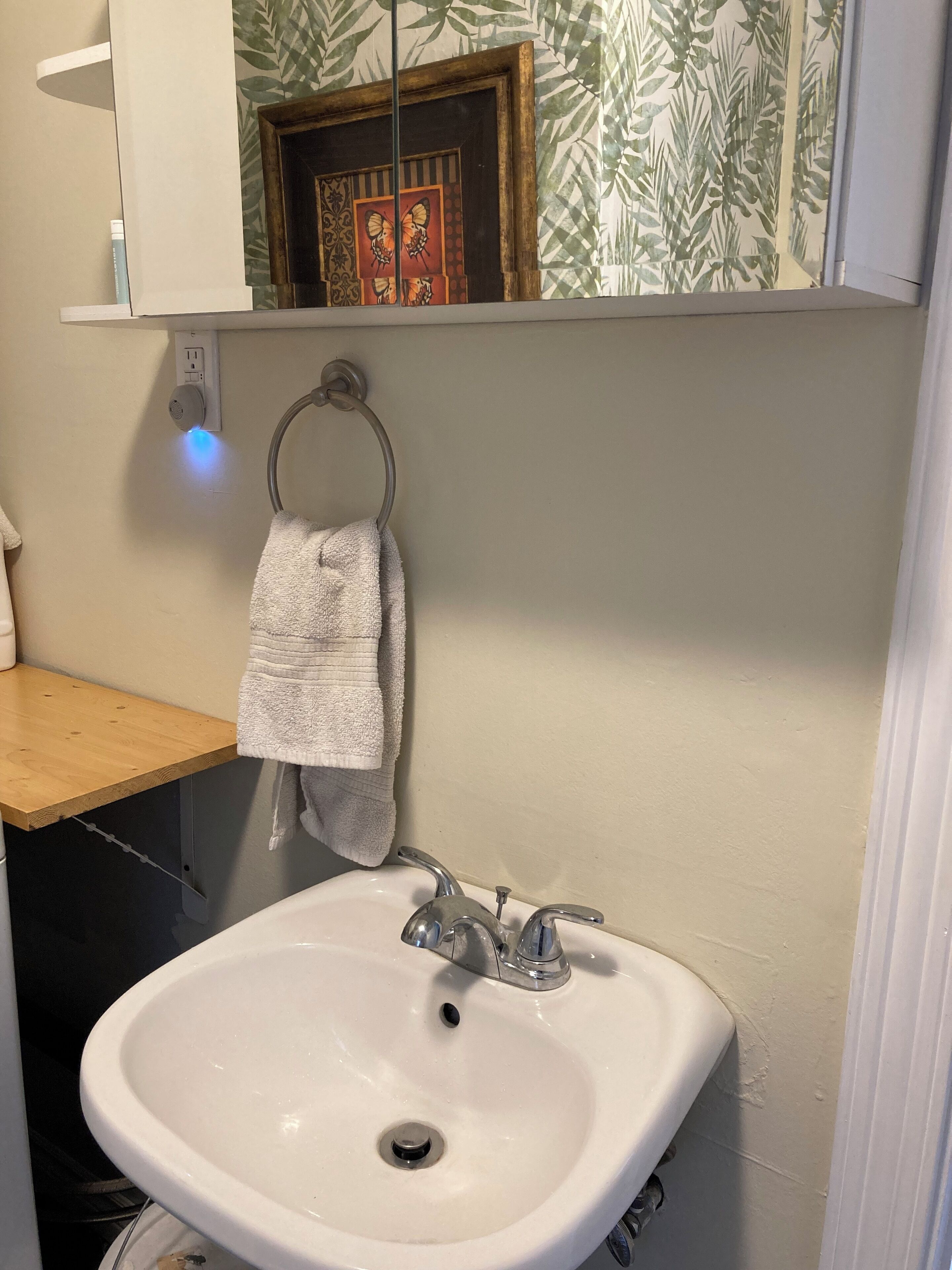 Een badkamer met een wit wastafelmeubel, een handdoek aan een metalen ring en een spiegel boven de wastafel.
