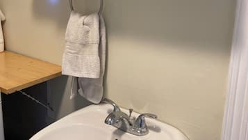 Een badkamer met een wit wastafelmeubel, een handdoek aan een metalen ring en een spiegel boven de wastafel.