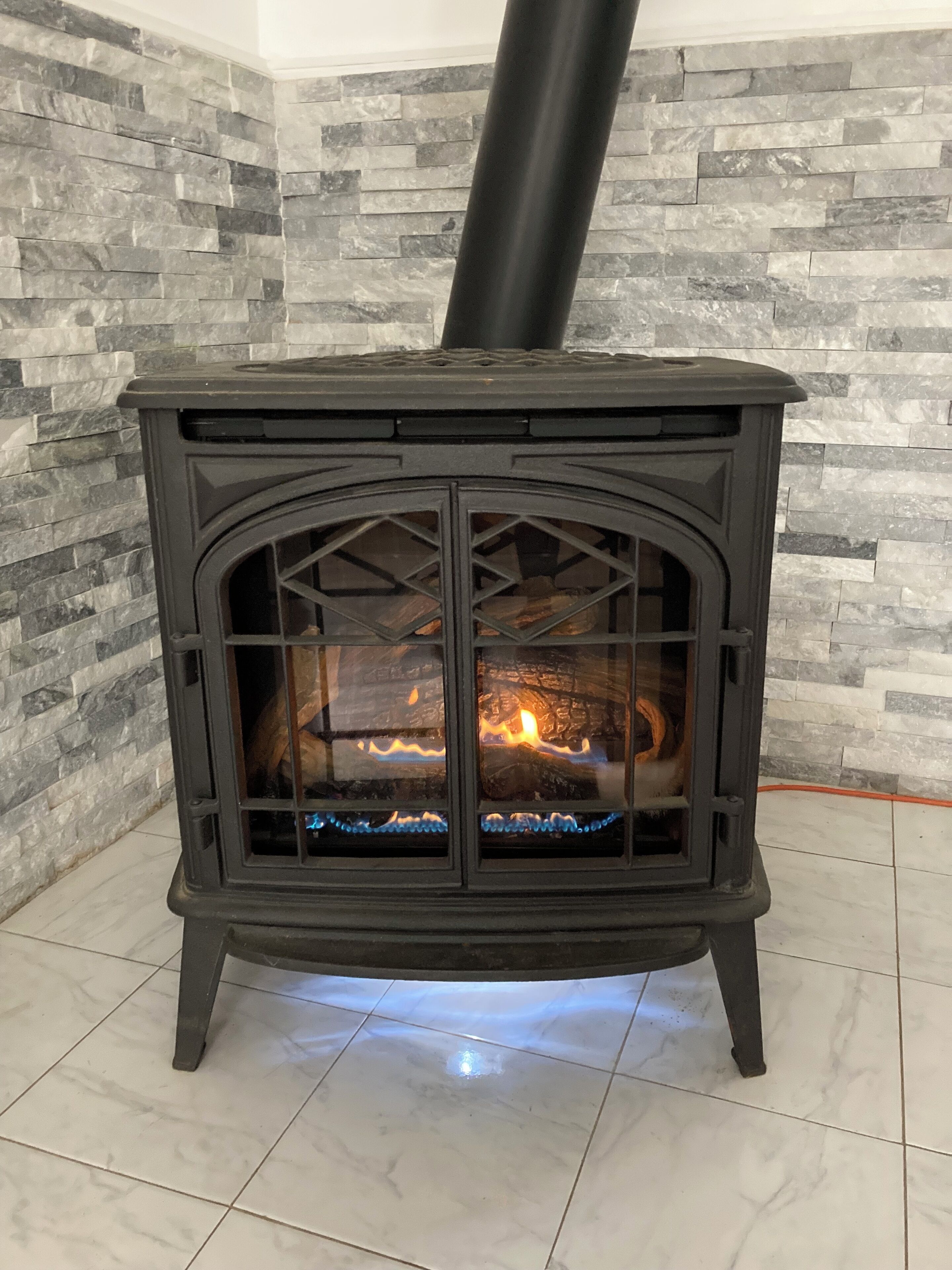 A wood-burning stove with a glass front, set against a stone wall.