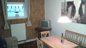 Una habitación pequeña con una mesa de madera, un televisor y una ventana con cortinas.