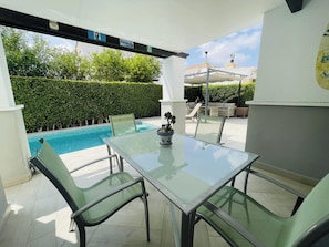 An outdoor patio with a glass table and chairs, a pool, and a covered seating area. - La Torre Golf 3-bed Villa- Pool, Hot Tub & Terrace (Torre-Pacheco)