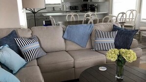 A living room with a beige sectional sofa, a round coffee table, and a vase with flowers.