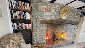 Ein gemütliches Wohnzimmer mit einem Kamin aus Stein, einem Holzregal voller Bücher und einem armchair mit Blumenmuster.