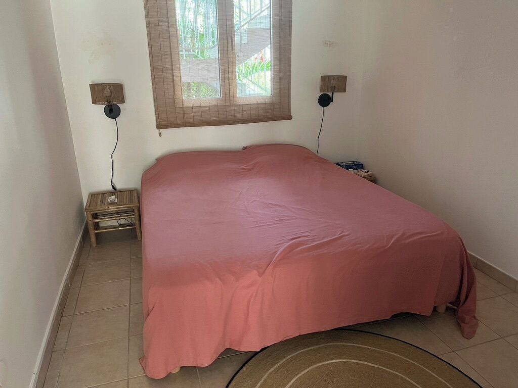 Ein Schlafzimmer mit einem Einzelbett, zwei Nachttischen, einem Fenster mit Jalousien und einer Steckdose.