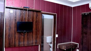 Un baño con tocador de madera, televisor montado y un inodoro.