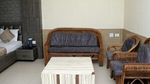 Una habitación con una cama, un sofá, dos sillones de mimbre y una mesa a rayas.