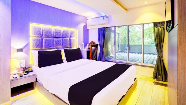 A modern hotel room with a large bed, a bedside table with a lamp, a phone, and a small table with a vase of flowers.