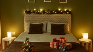 Una cama bien hecha con un árbol de Navidad y regalos, un cabecero estampado y marcos de cuadros colgados en la pared.