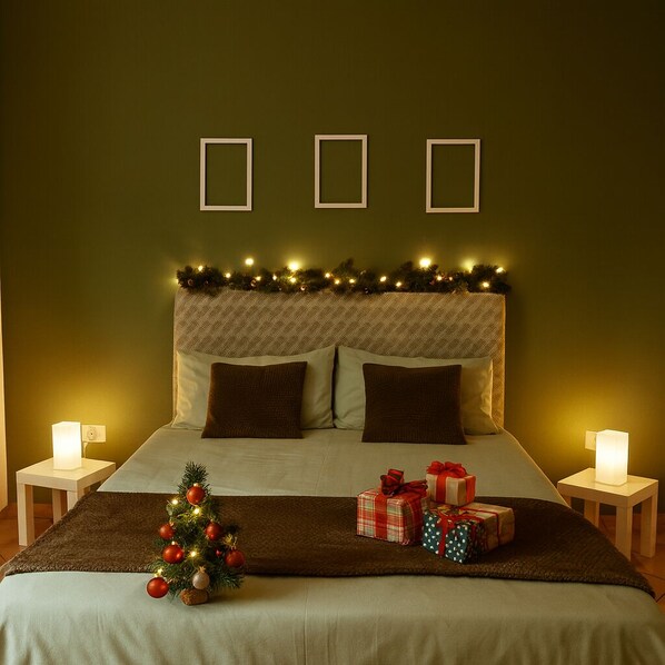 A neatly made bed with a Christmas tree and presents, a patterned headboard, and wall-mounted picture frames.