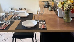 Un comedor con una mesa de madera preparada para dos comensales, un jarrón de flores y un reloj de pared.