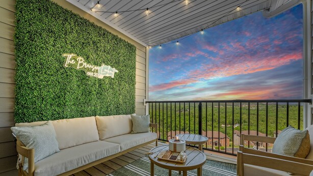 Un balcón con un muro verde, un sofá, una mesa y vistas al cielo.
