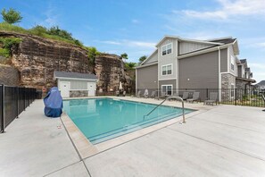 A swimming pool with a covered area, a building with a stone facade, and a fenced patio area.