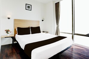 A hotel room with a large bed, a bedside table, a nightstand, a framed picture on the wall, and a window with curtains.