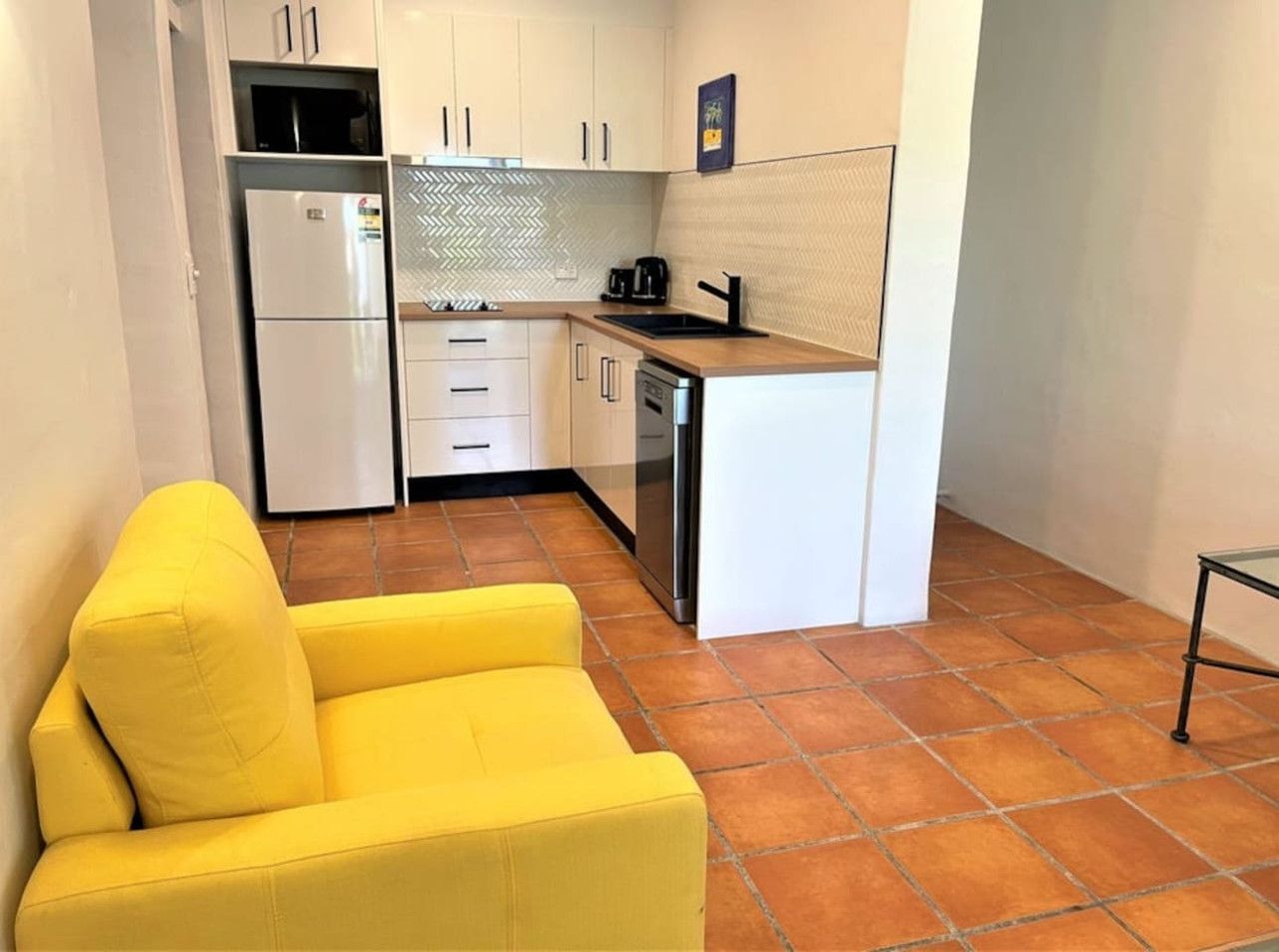 Una cucina compatta con mobili bianchi, un forno a microonde integrato, una macchina da caffè e un lavandino.