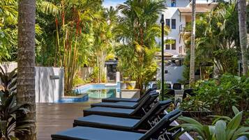 A poolside area with lounge chairs, a pool, and a building with a tiled roof.
