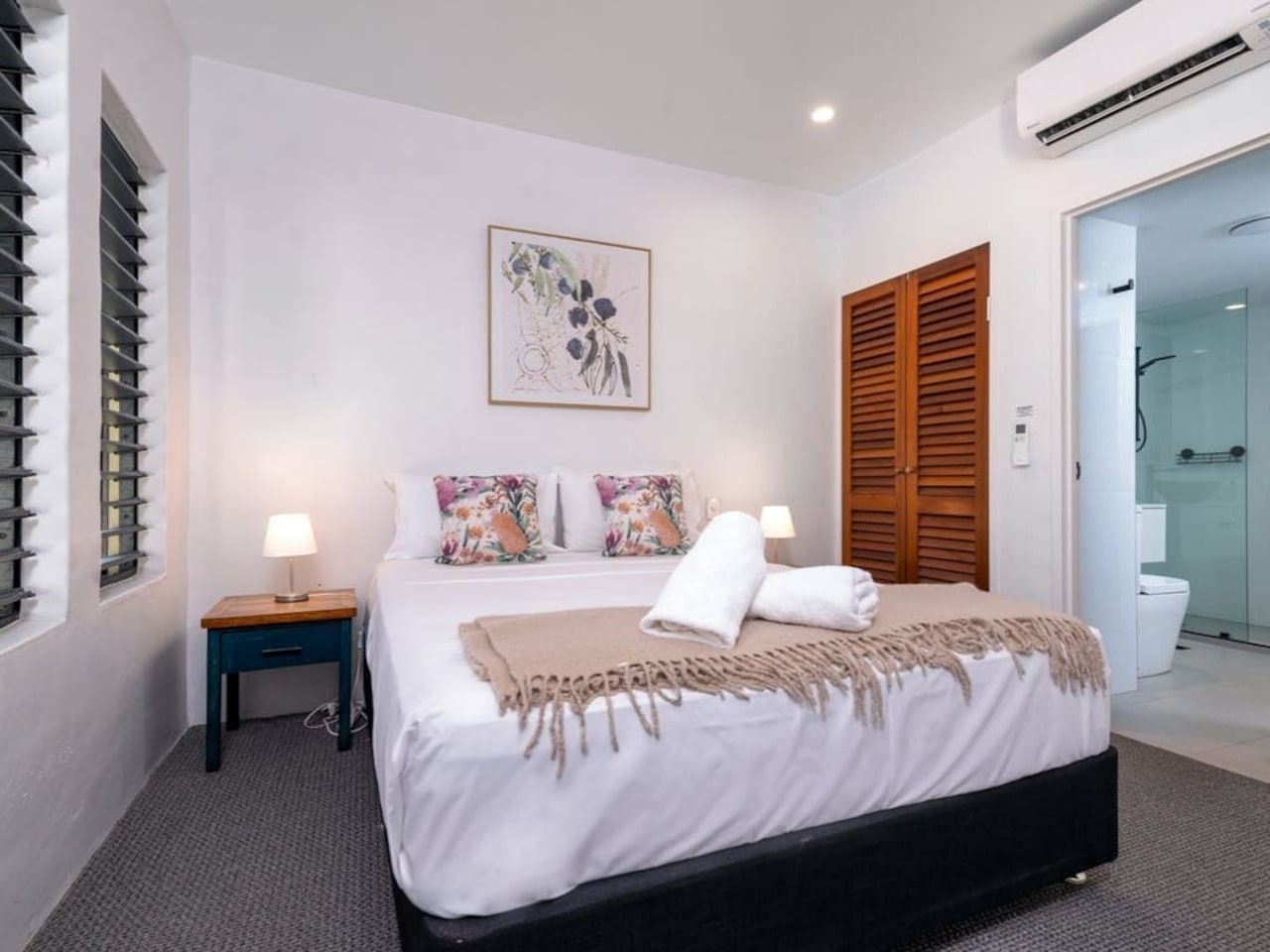 Una camera d'albergo con un letto, comodini, una doccia e una porta vetrata che dà sul bagno.