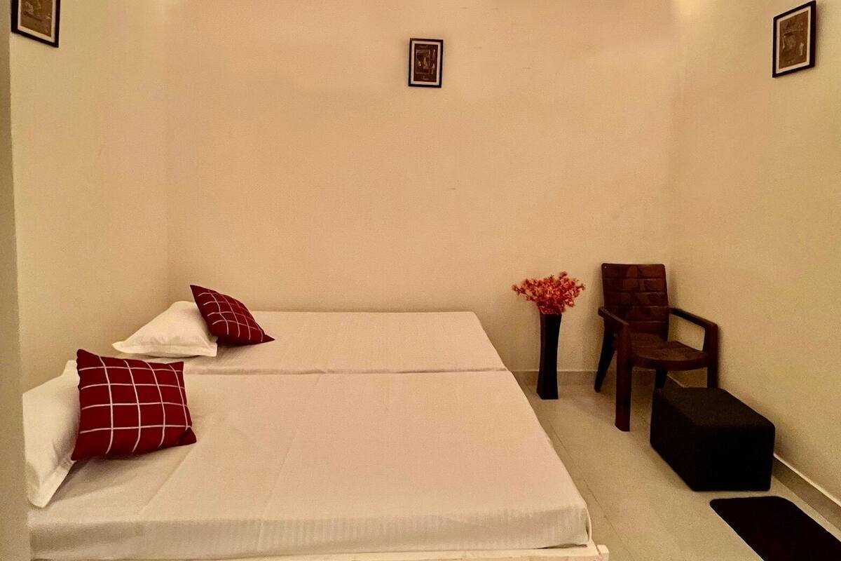 A bedroom with a single bed, a ceiling fan, string lights, a chair, and a small table.