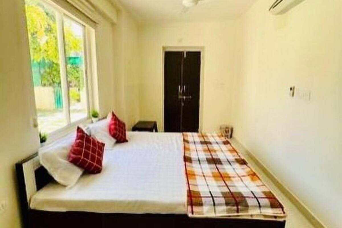 A bedroom with a bed, a window, a door, and an air conditioning unit.