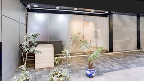 Un espace d’accueil moderne avec une porte en verre, un banc en bois et des plantes en pot.