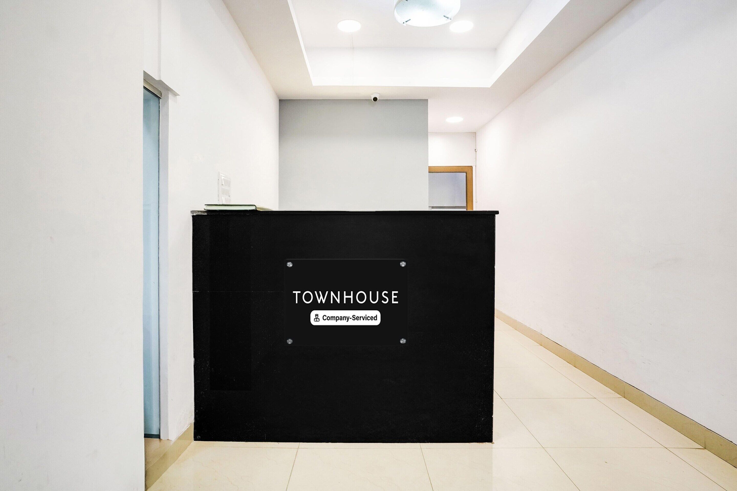 A reception desk labeled "TOWNHOUSE" with a "Company-Serviced" sign, a door to the left, and a ceiling with recessed lighting.