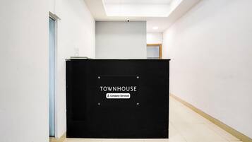 A reception desk labeled "TOWNHOUSE" with a "Company-Serviced" sign, a door to the left, and a ceiling with recessed lighting.