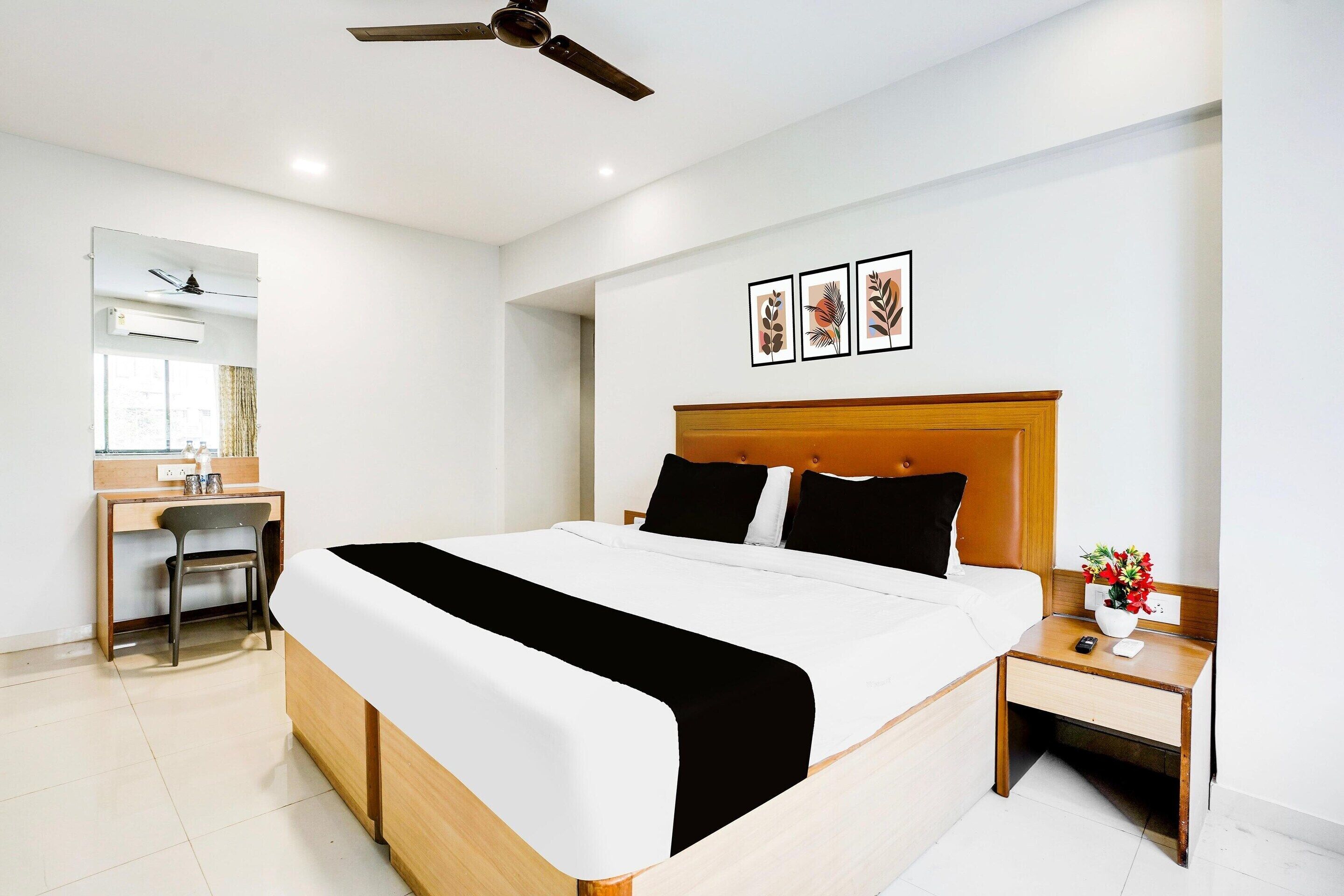 A hotel room with a bed, a desk, a chair, a nightstand, and a ceiling fan.