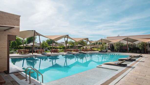Une piscine entourée d’un bâtiment en briques et de verdure, avec des chaises longues et des parasols à proximité.