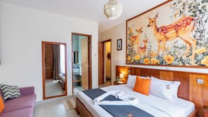 Une chambre d’hôtel avec un grand lit, un miroir, un tableau représentant des cerfs et un canapé violet.