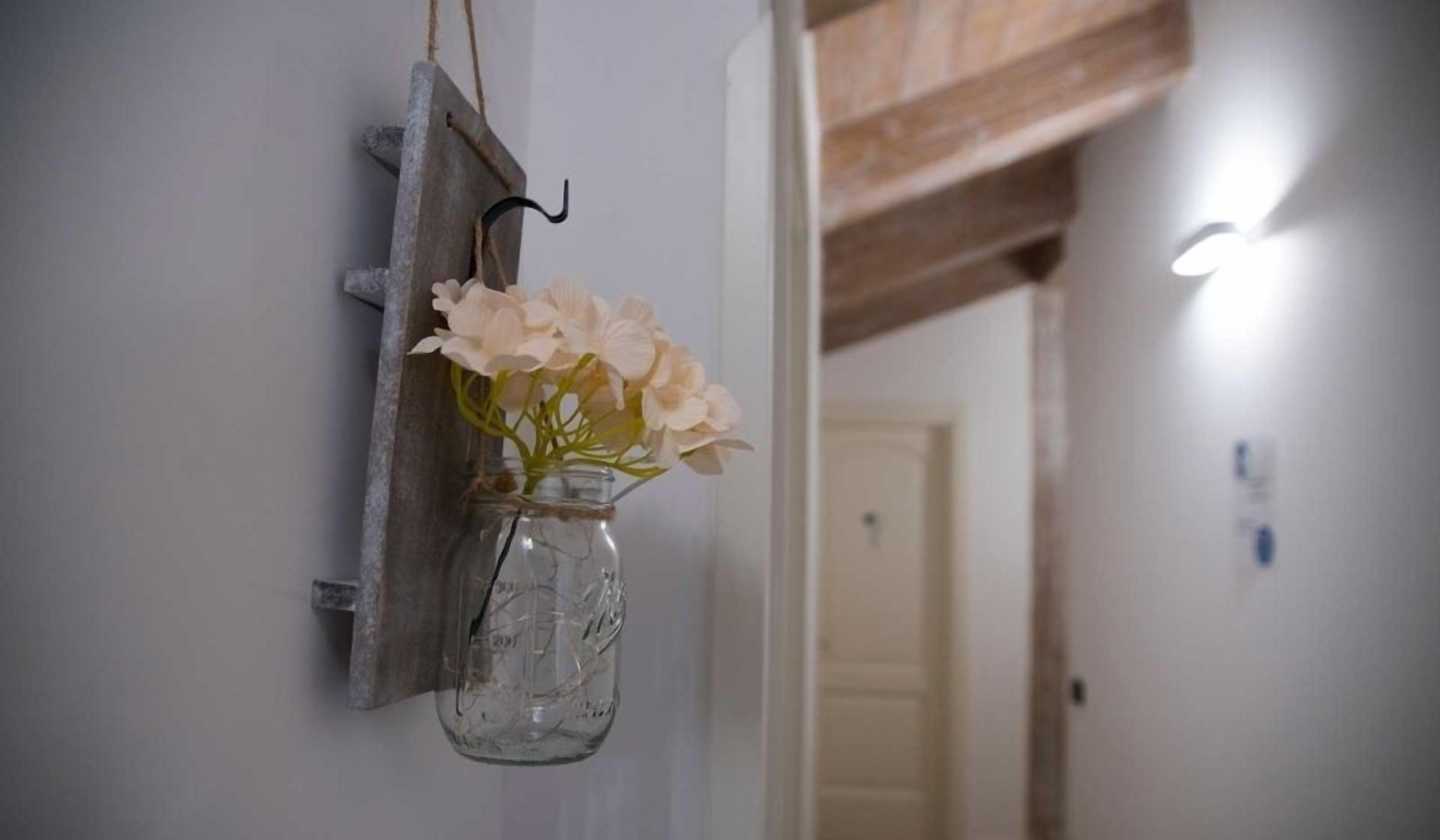 Una estantería rústica de pared con un frasco de vidrio transparente que contiene flores pálidas.
