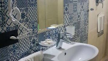 A bathroom with a white sink, a mirror, and a hairdryer on the wall.