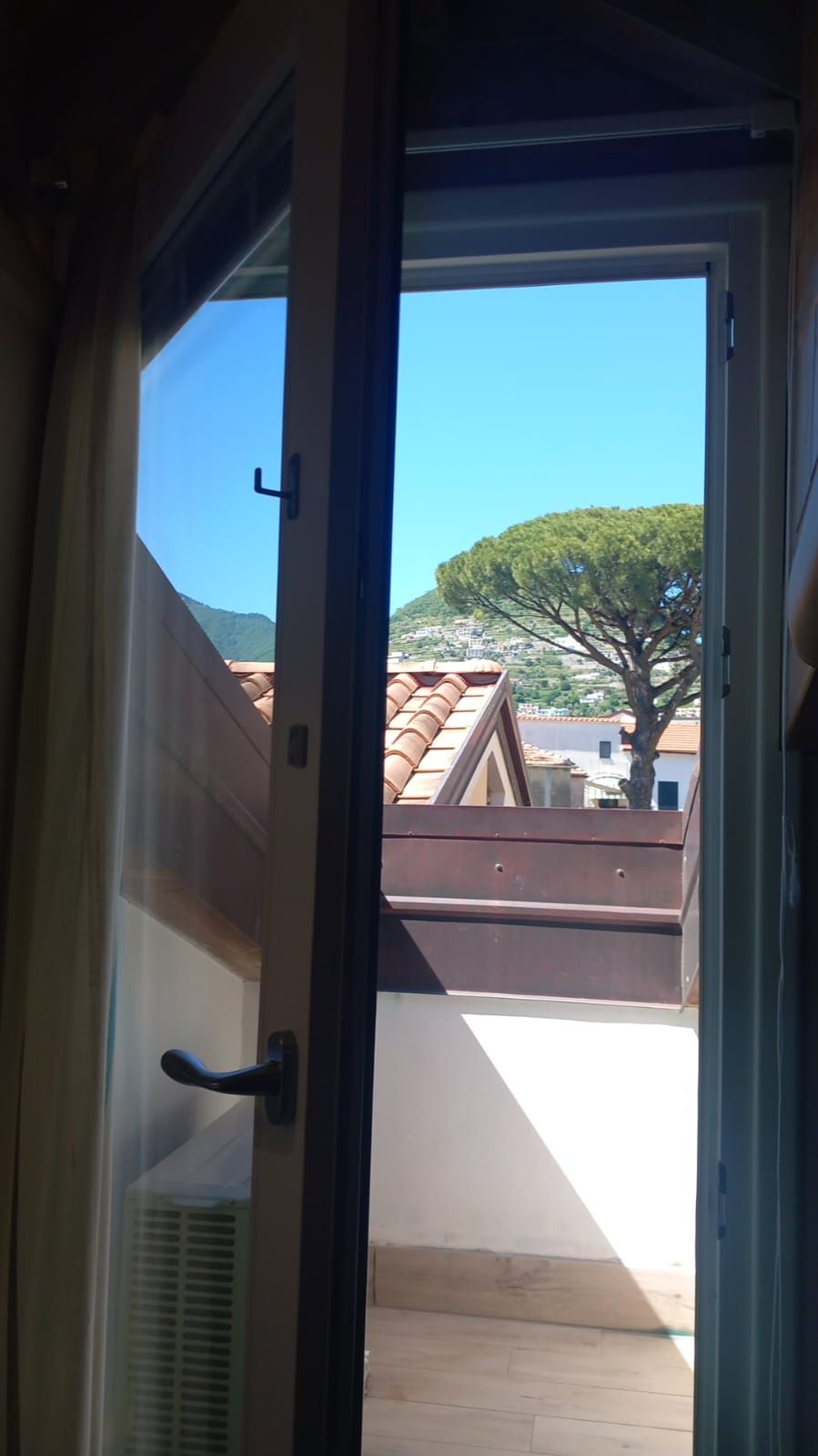 Une porte donnant sur un toit recouvert de tuiles, un arbre et, au loin, une colline.