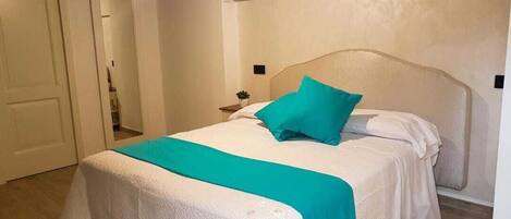 Una cama bien hecha con un edredón blanco y aguamarina, una almohada aguamarina y un cabecero de madera.