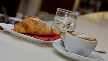 Un cornetto su un piatto bianco, un bicchiere d'acqua e una tazza di caffè su un piattino.