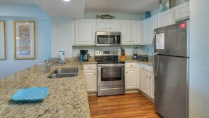 A modern kitchen with white cabinets, stainless steel appliances, a granite countertop, and a wooden floor. - Grand Atlantic 1407- Oceanfront - Indoor/Outdoor Pools (Myrtle Beach)