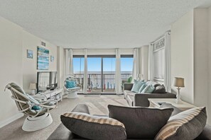 A spacious living room with a balcony, a comfortable sofa set, and a dining area. - Springs 206-Oceanfront 3BR in Cherry Grove-Pool (North Myrtle Beach)