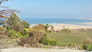 Un paysage côtier offrant une vue dégagée sur l’océan, une zone herbeuse et un sentier de pierres menant à la plage.