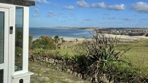 Une vue sur la côte, prise depuis un bâtiment doté d’un mur en pierre et d’une végétation au premier plan, donnant sur une plage et un paysage lointain.