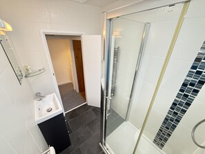 Une salle de bain moderne avec une douche à l’italienne en verre, un lavabo blanc et un sol carrelé foncé.
