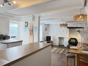 Une cuisine moderne avec un îlot central en bois, une cheminée en pierre et un coin repas comprenant une table et des chaises.