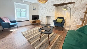Een woonkamer met een stenen muur, een open haard, een televisie en twee fauteuils.