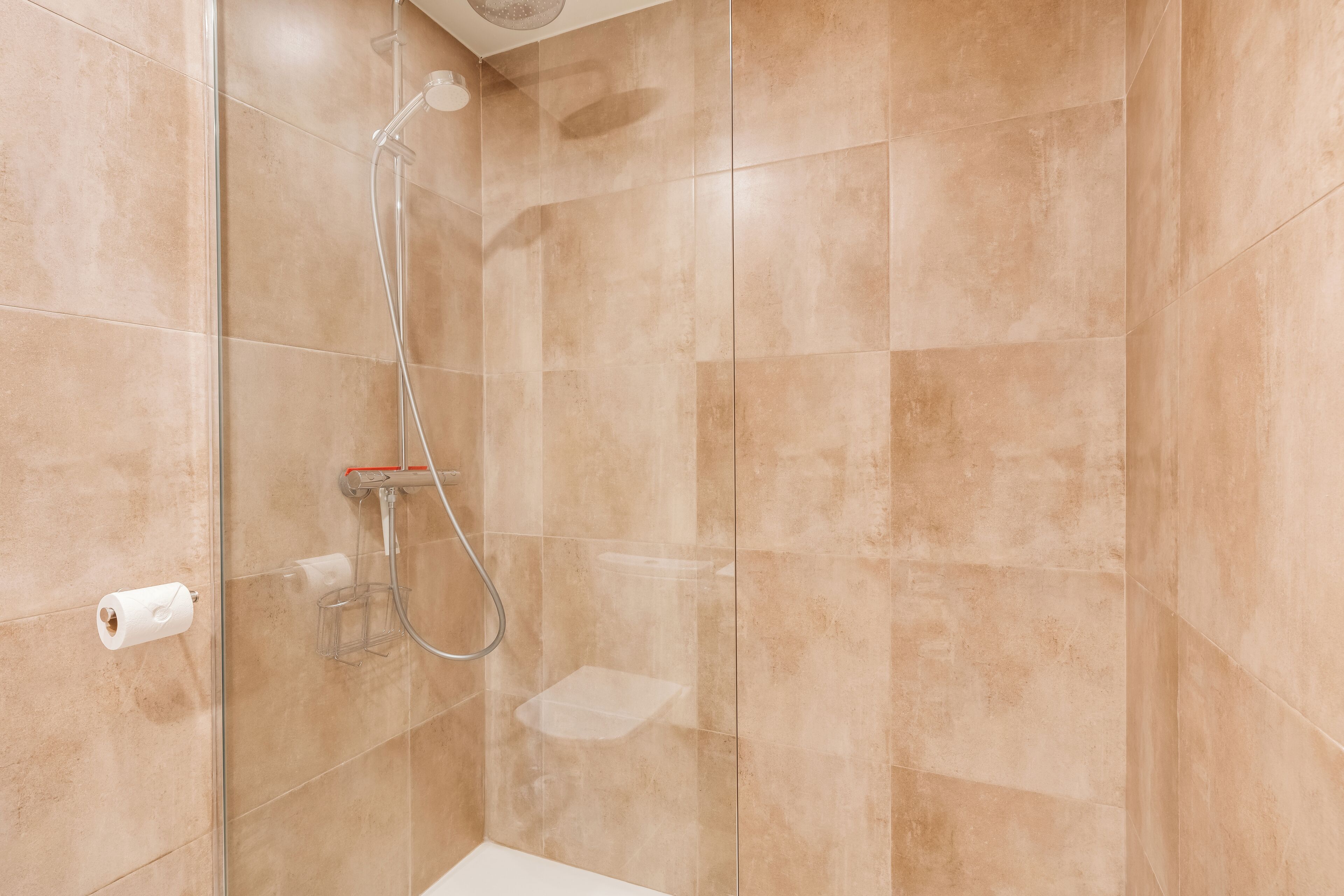 Een douche met beige tegels, een glazen deur en een handdouche.