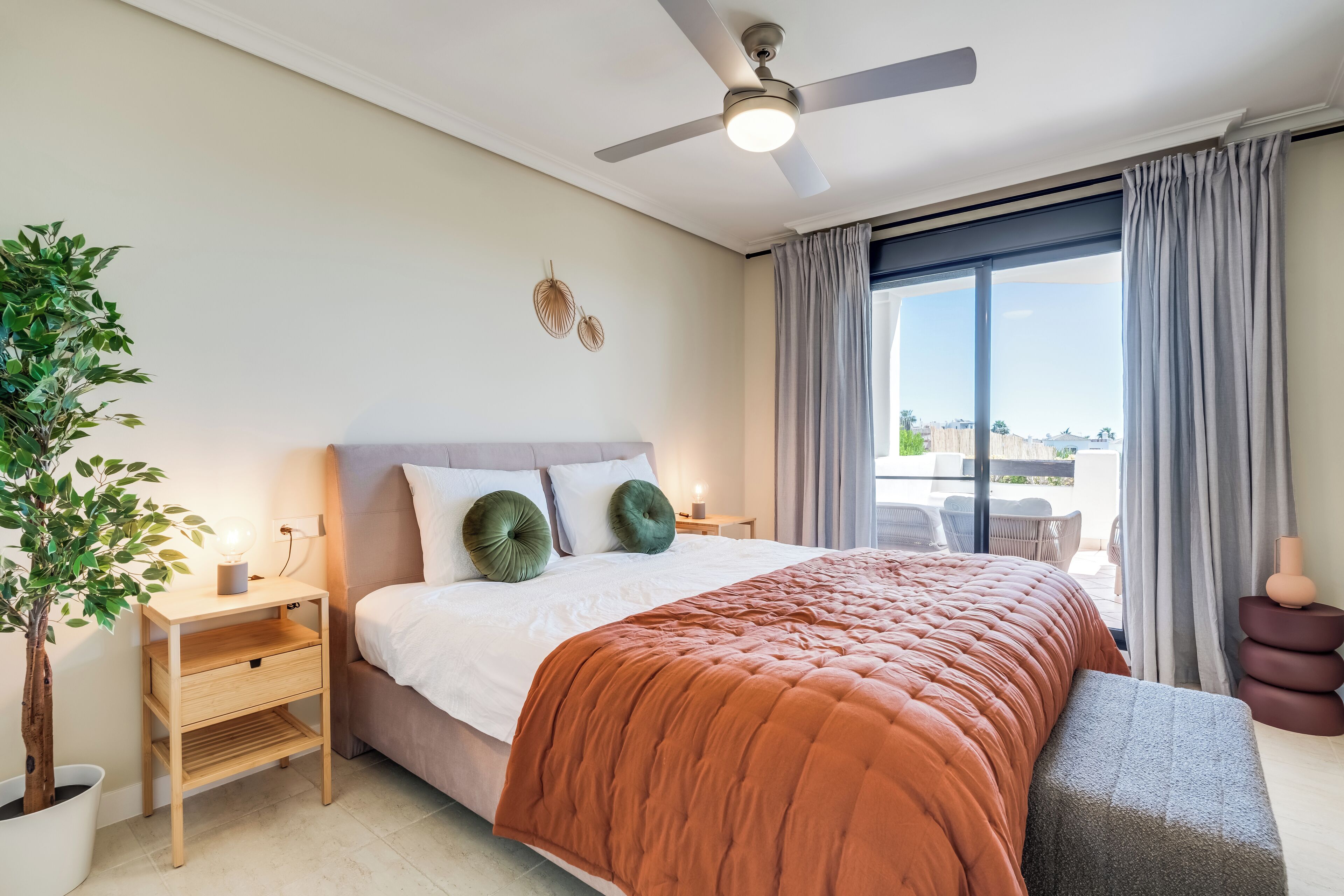 Un dormitorio moderno con una cama grande, ventilador de techo, planta en maceta y vistas al exterior.